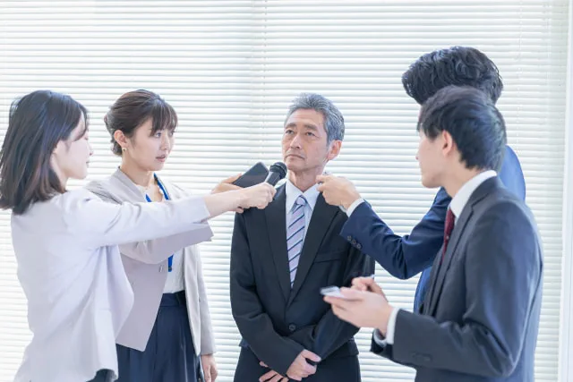 会見で皆に囲まれる会社員